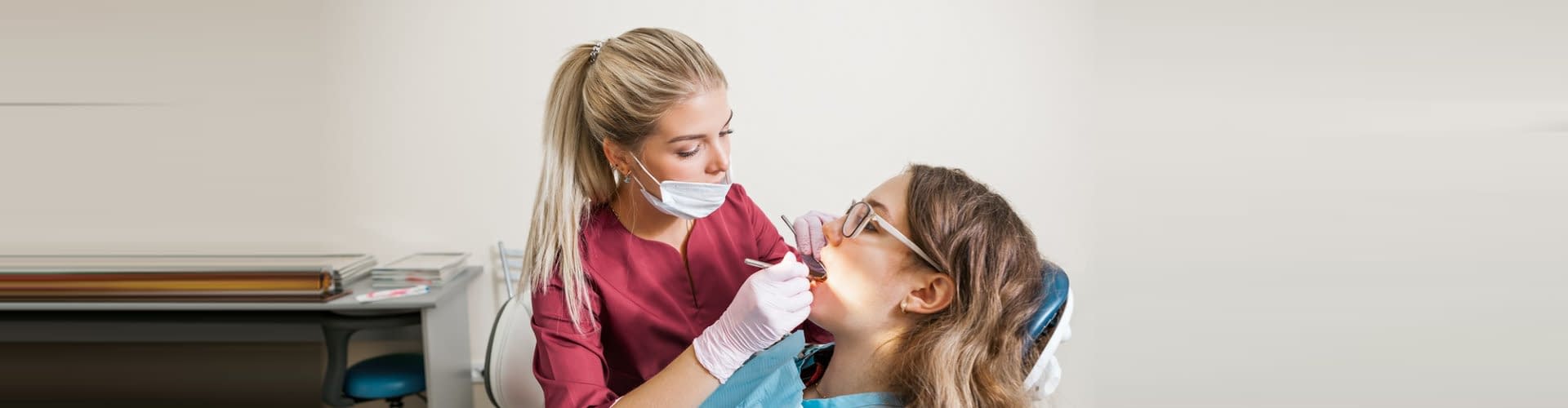 beautiful women dentist in the mask examines a patient in the dental office